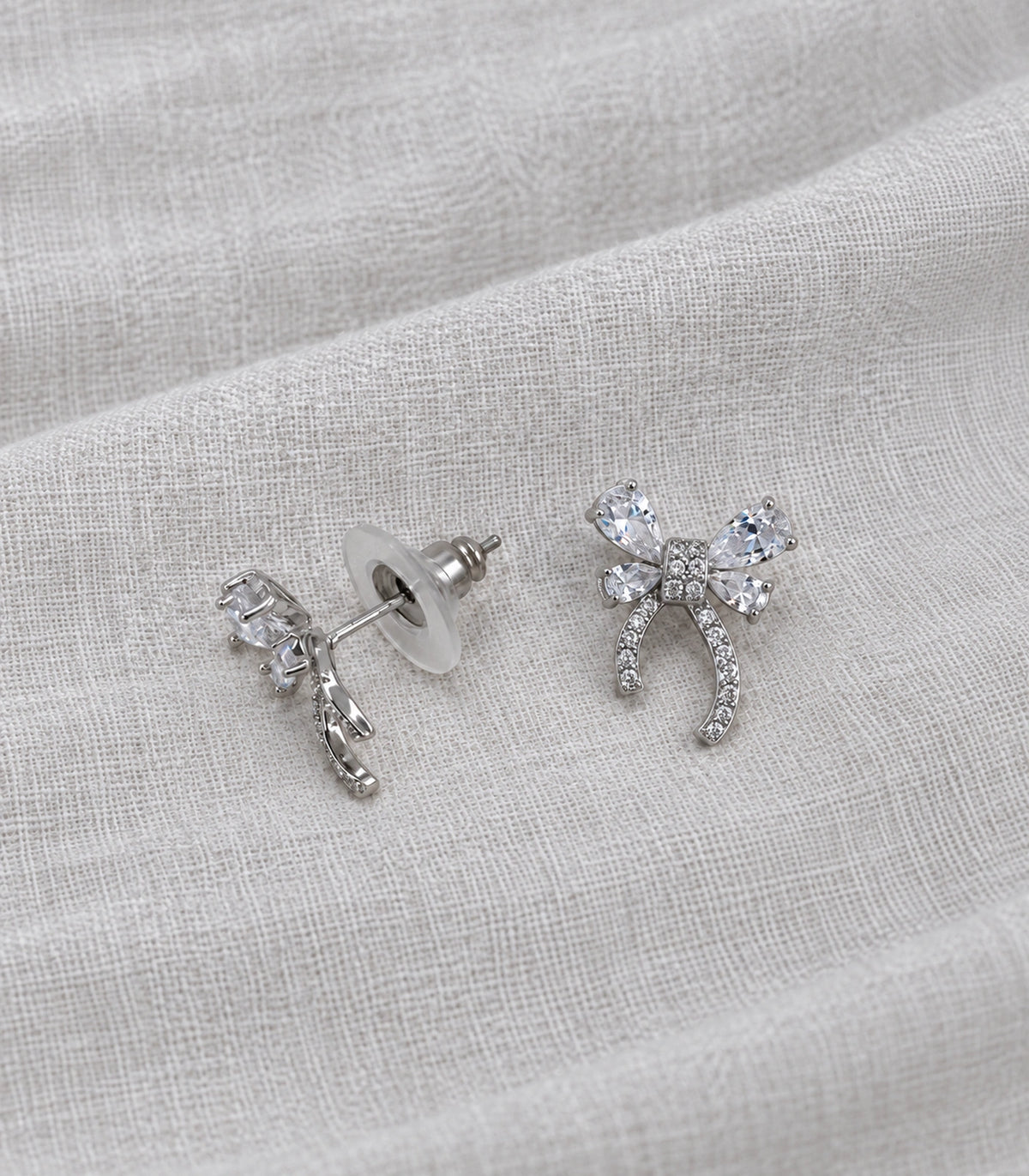 JIMIKI Four Pear Crystal Bow Stud Earring Pair in Silver Tone, editorial flat lay #color_silver tone