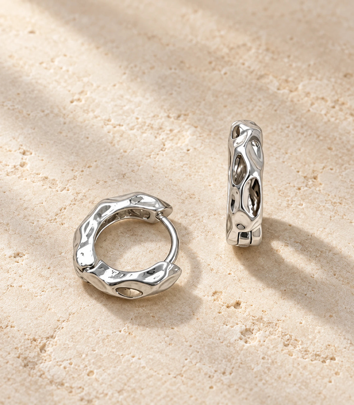 JIMIKI Silver Hammered Marquise Cutout Huggie Hoop Earrings, matching pair on a textured stone surface #color_silver
