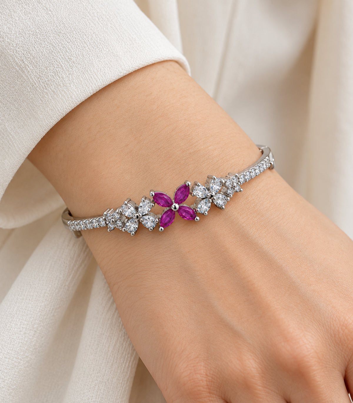 Close view of the magenta four-petal centre and clear floral settings of one silver-tone bangle