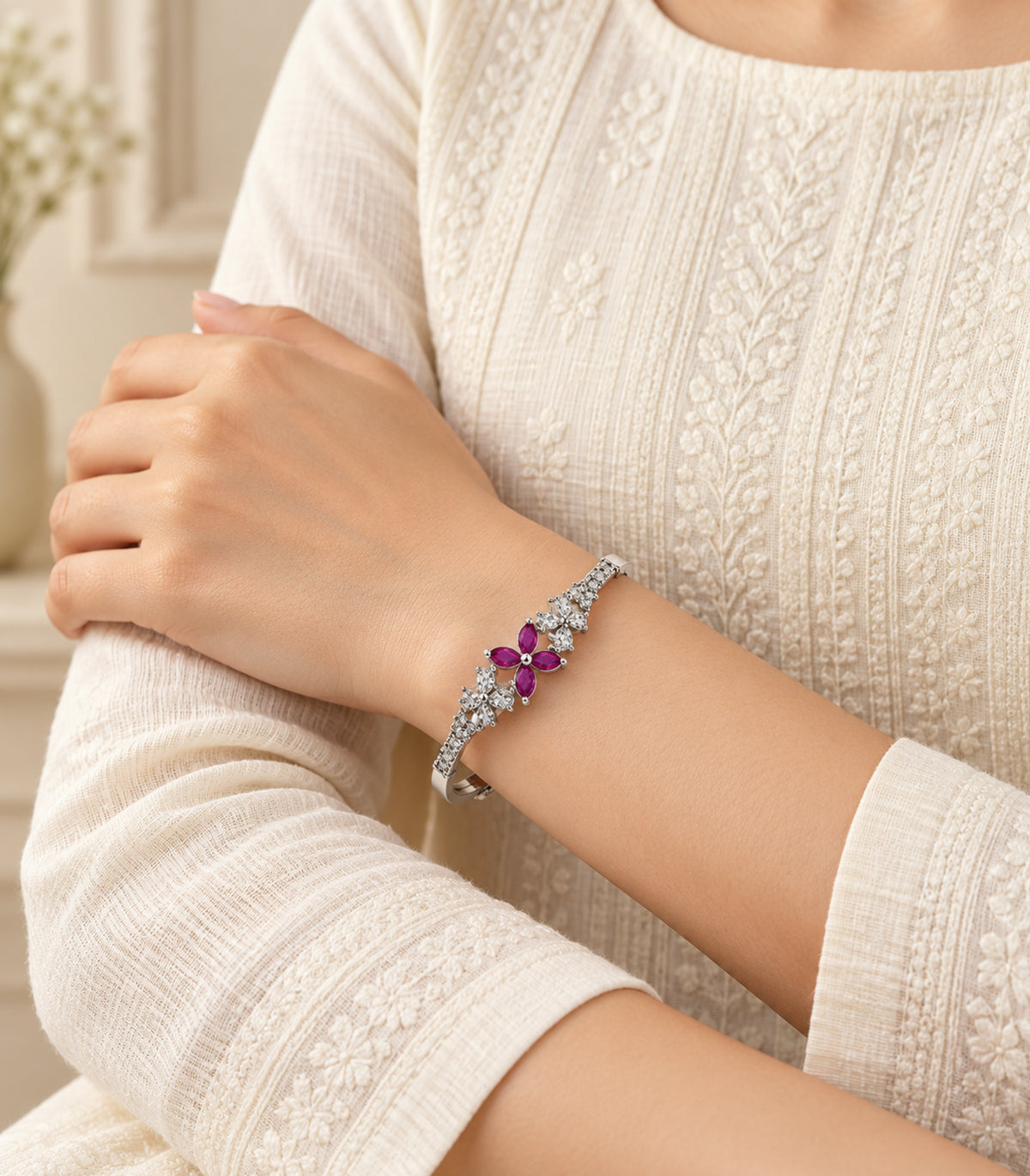 Editorial wrist view of one silver-tone bangle with magenta petals and clear flower clusters