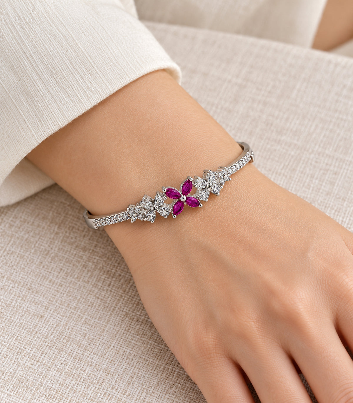Silver-tone magenta four-petal and clear flower bangle worn on a wrist