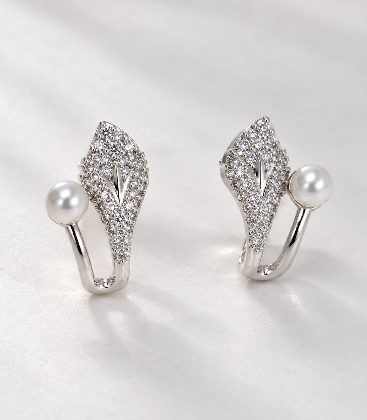 Close detail of the matching silver-tone leaf and pearl-style earrings on fabric