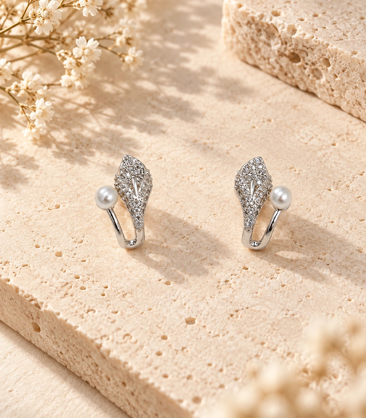 Matching pair of silver-tone leaf and pearl-style earrings in a styled flatlay