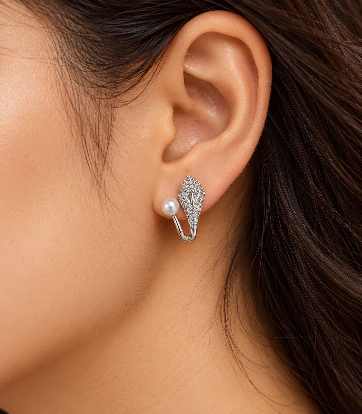 Editorial ear view of a silver-tone pavé leaf and white pearl-style ear jacket earring