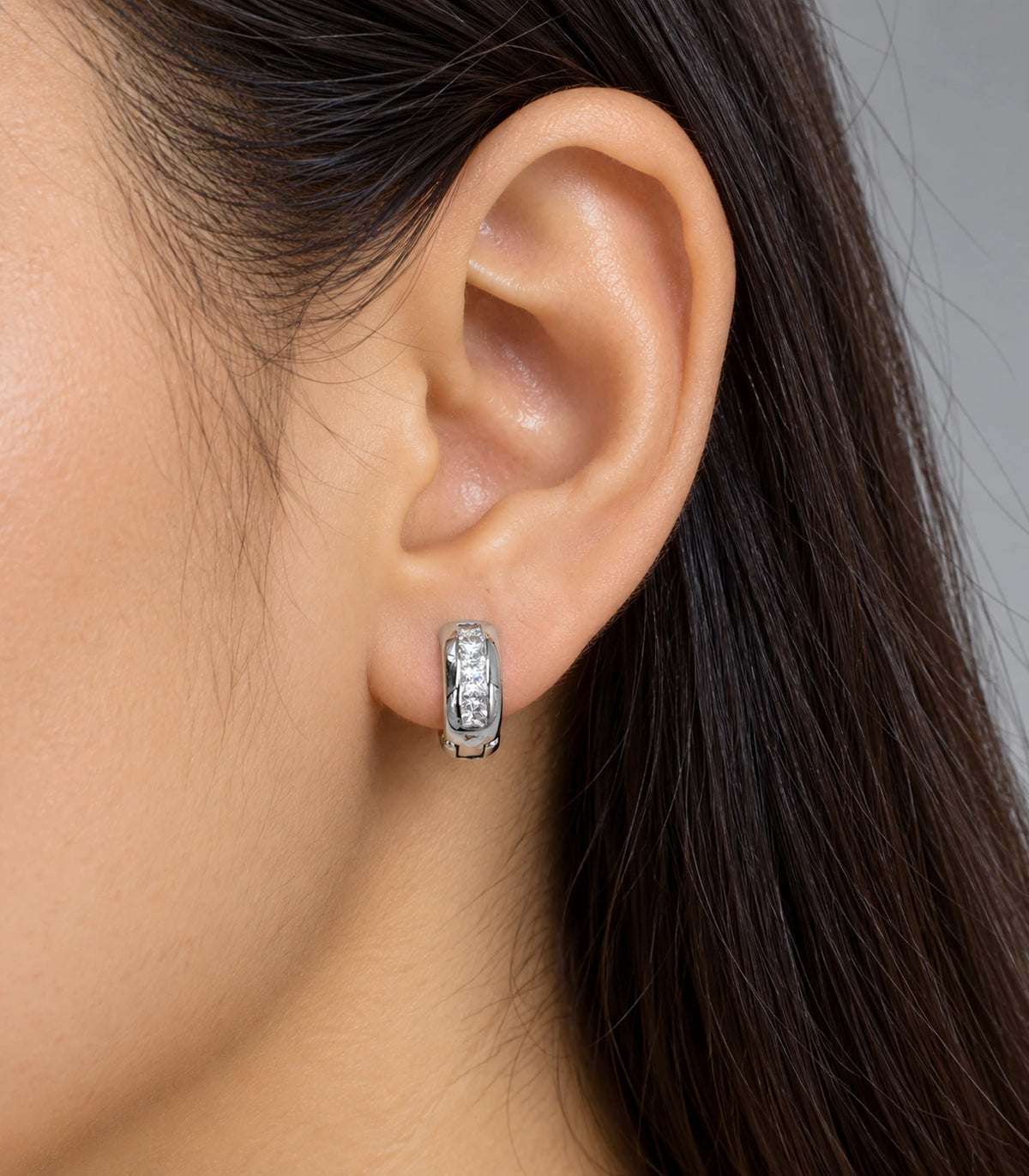 JIMIKI Silver Rectangular Crystal Channel Huggie Hoop Earrings, shown worn on the ear #color_silver