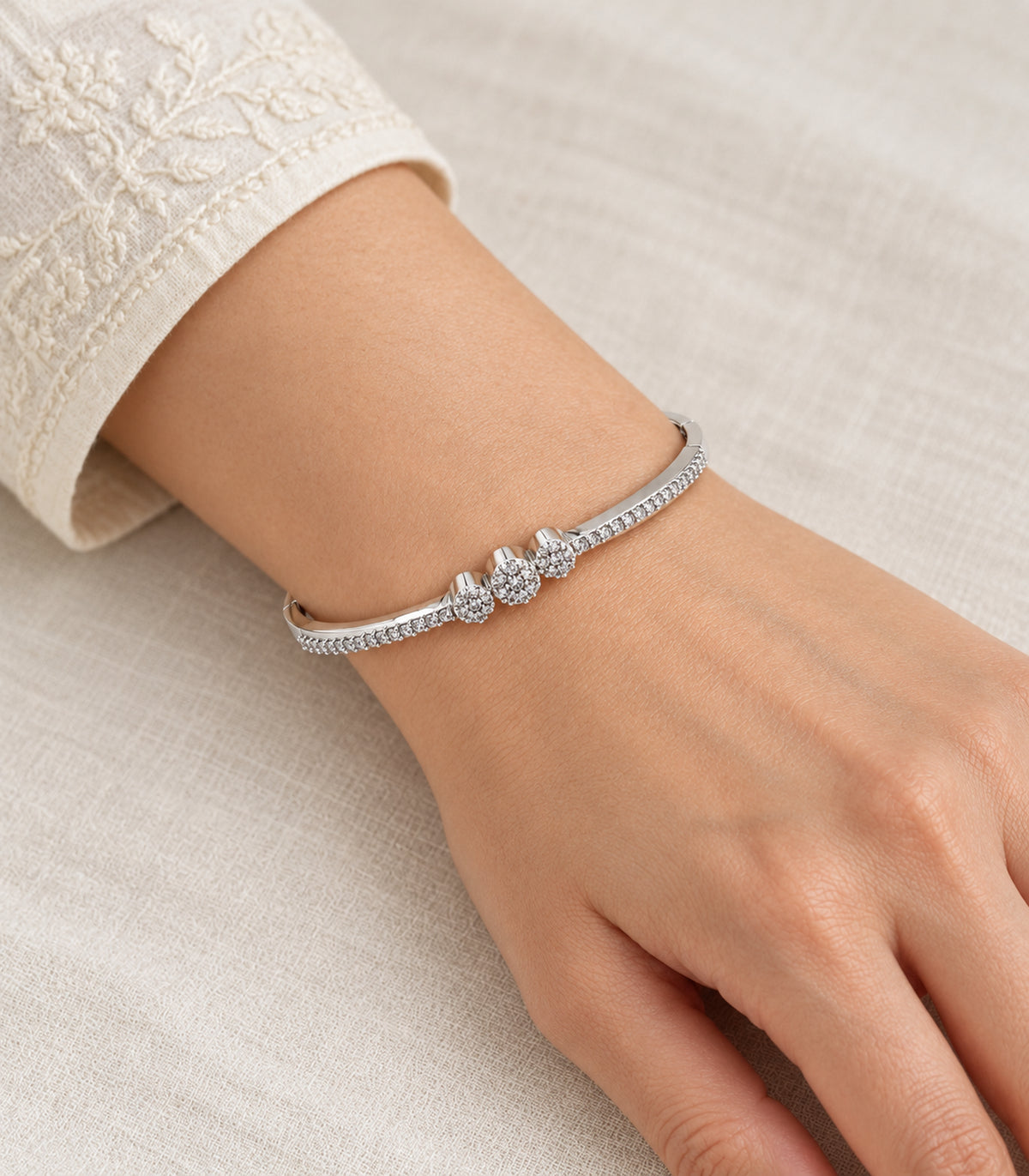 Silver-tone three-flower crystal bangle worn on a wrist beside an ivory sleeve