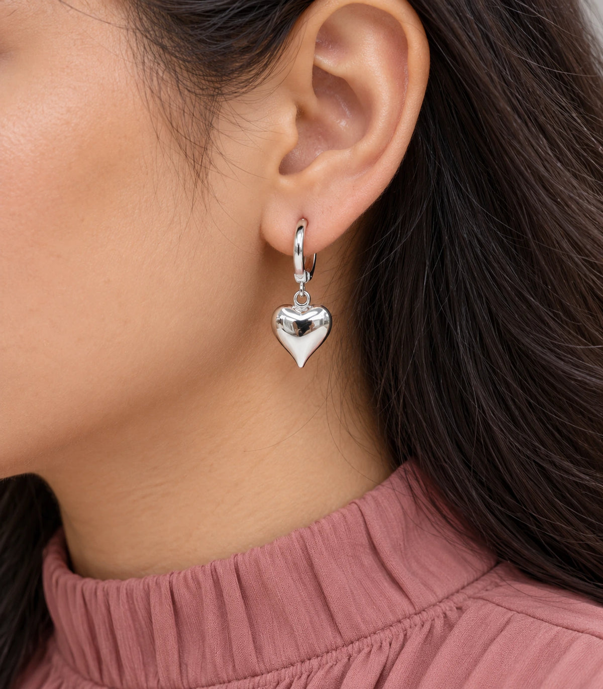 Close view of the smooth pointed-heart silver-tone hoop earring worn naturally