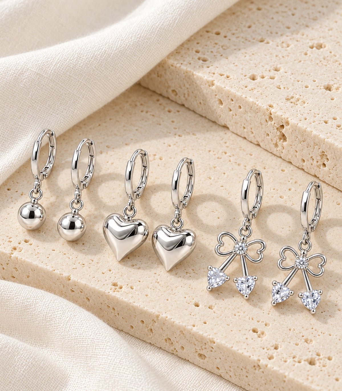 Complete six-earring silver-tone ball, heart and crystal bow set arranged on stone and linen