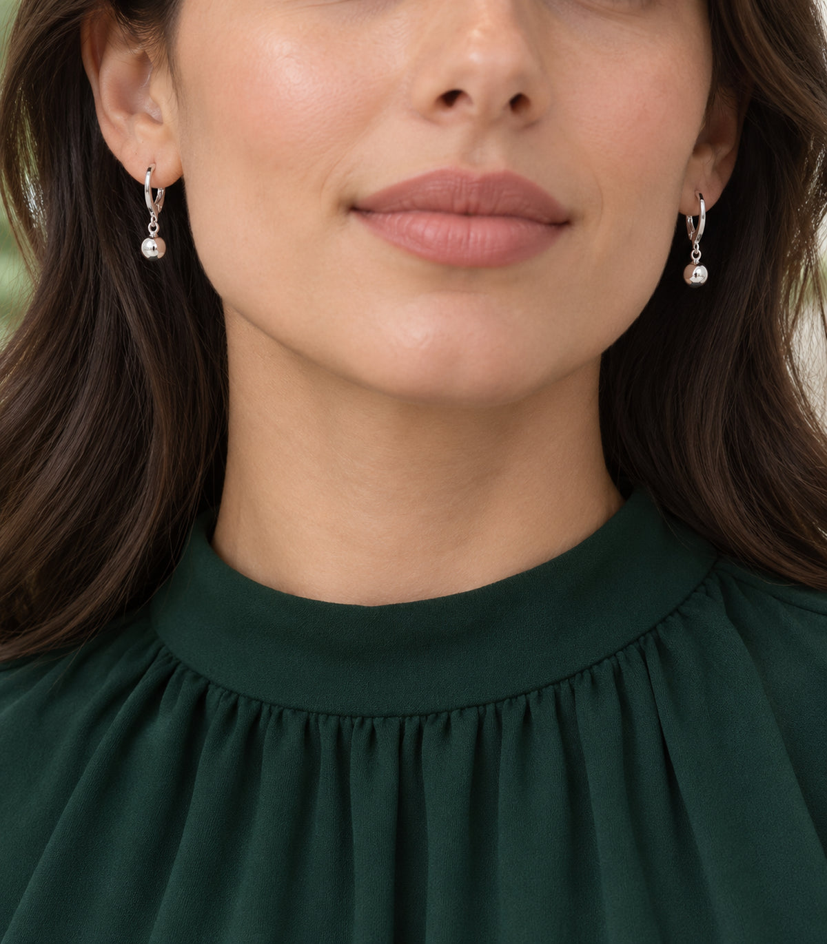 Silver-tone ball charm hoop earring pair worn with dark-green high-neck clothing