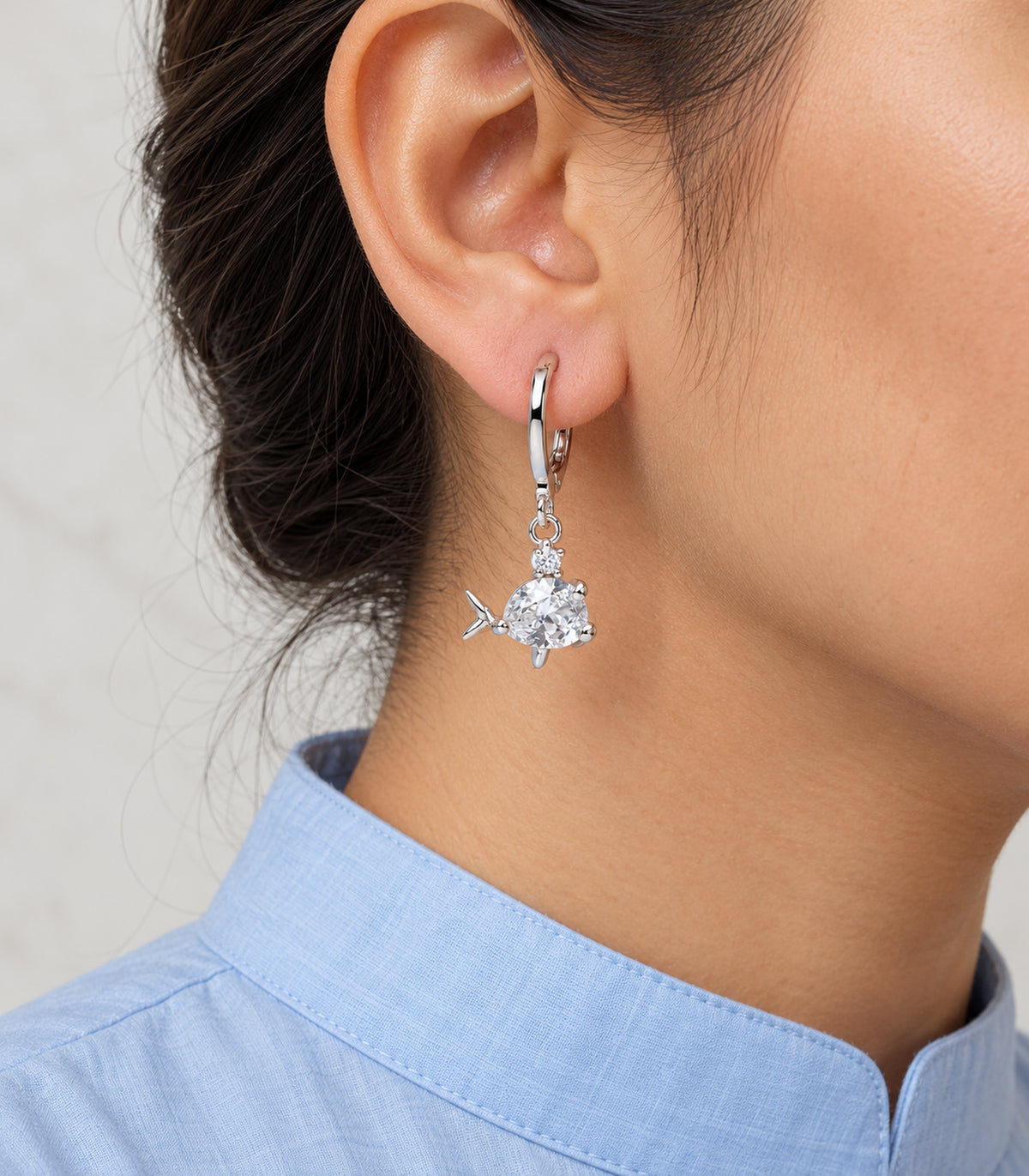 Clear pear-body fish charm hoop with small top stone and forked tail, worn detail.