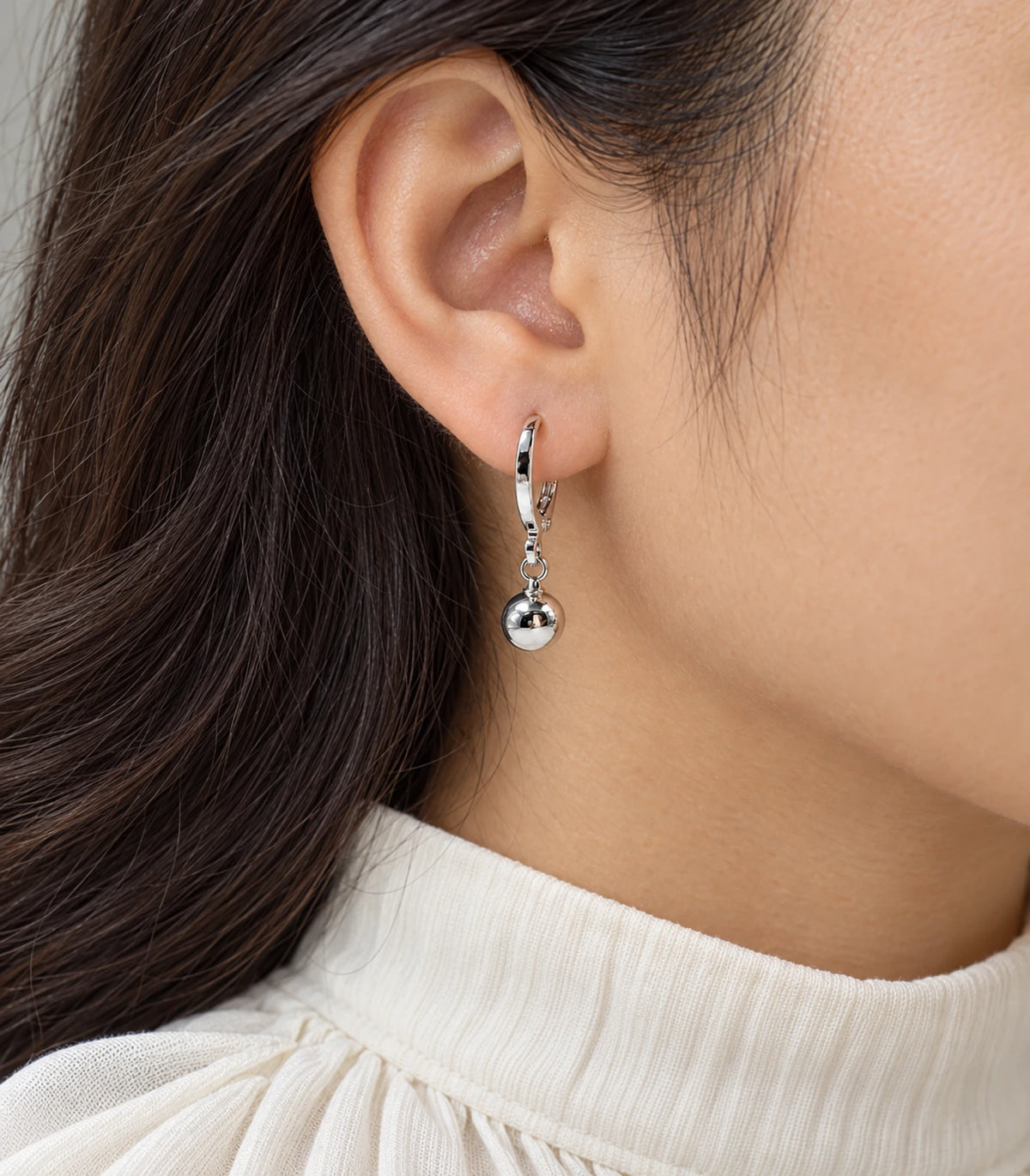 Polished silver-tone ball charm hoop earring shown in closeup