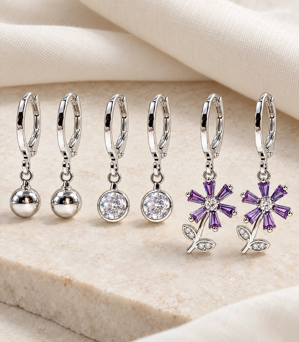 Complete three-pair silver-tone hoop earring set arranged on stone and linen