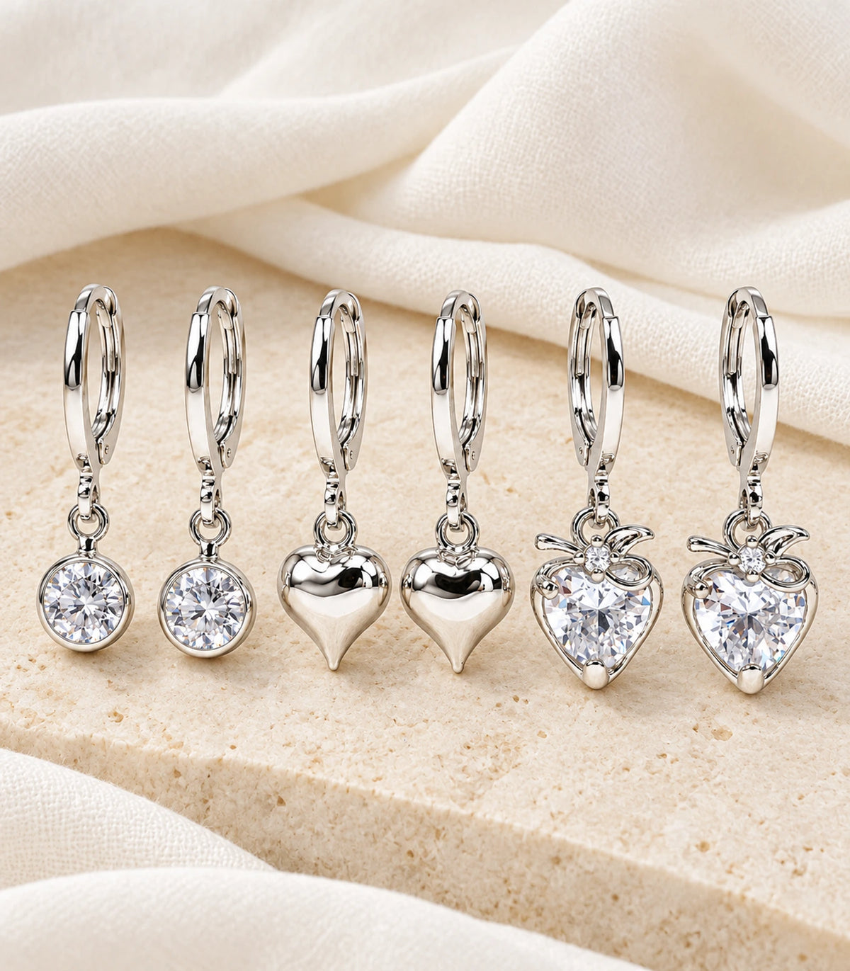 All six silver-tone hoops in the three-pair crystal and heart set arranged on linen and stone