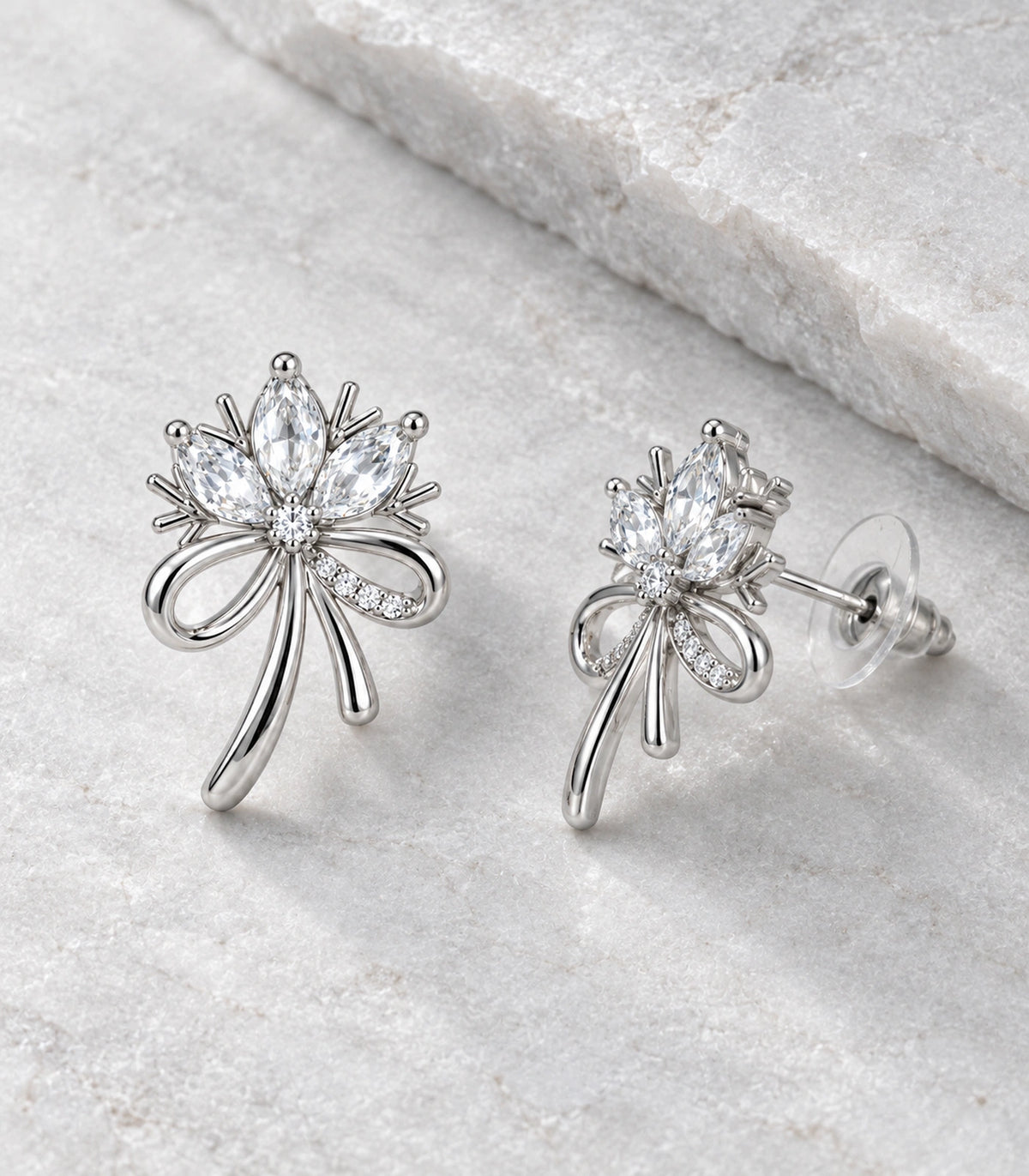 JIMIKI Silver-Tone Three-Petal Crystal Flower Bow Stud Earrings in Silver / Clear, editorial flat lay
