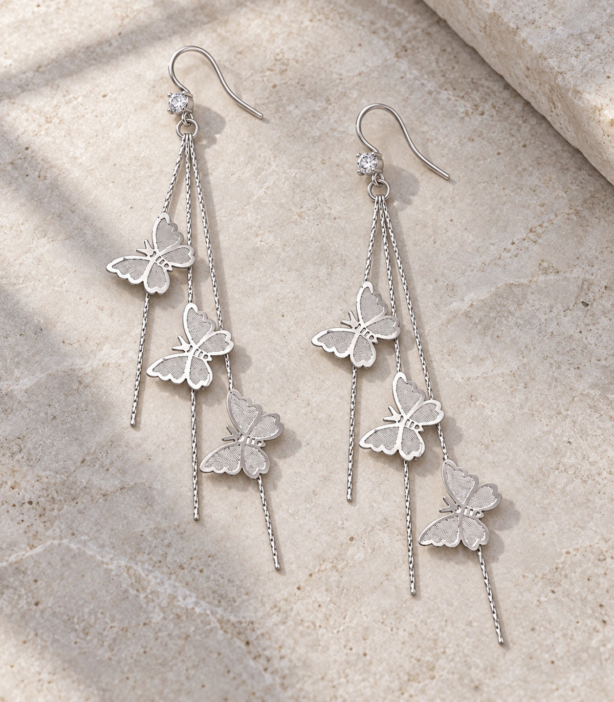 JIMIKI Silver-Tone Triple Butterfly Chain Drop Earrings in Silver Tone, editorial flat lay