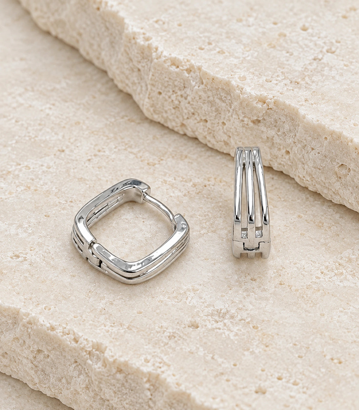 JIMIKI Silver Triple Open Rail Huggie Hoop Earrings, matching pair on a textured stone surface #color_silver