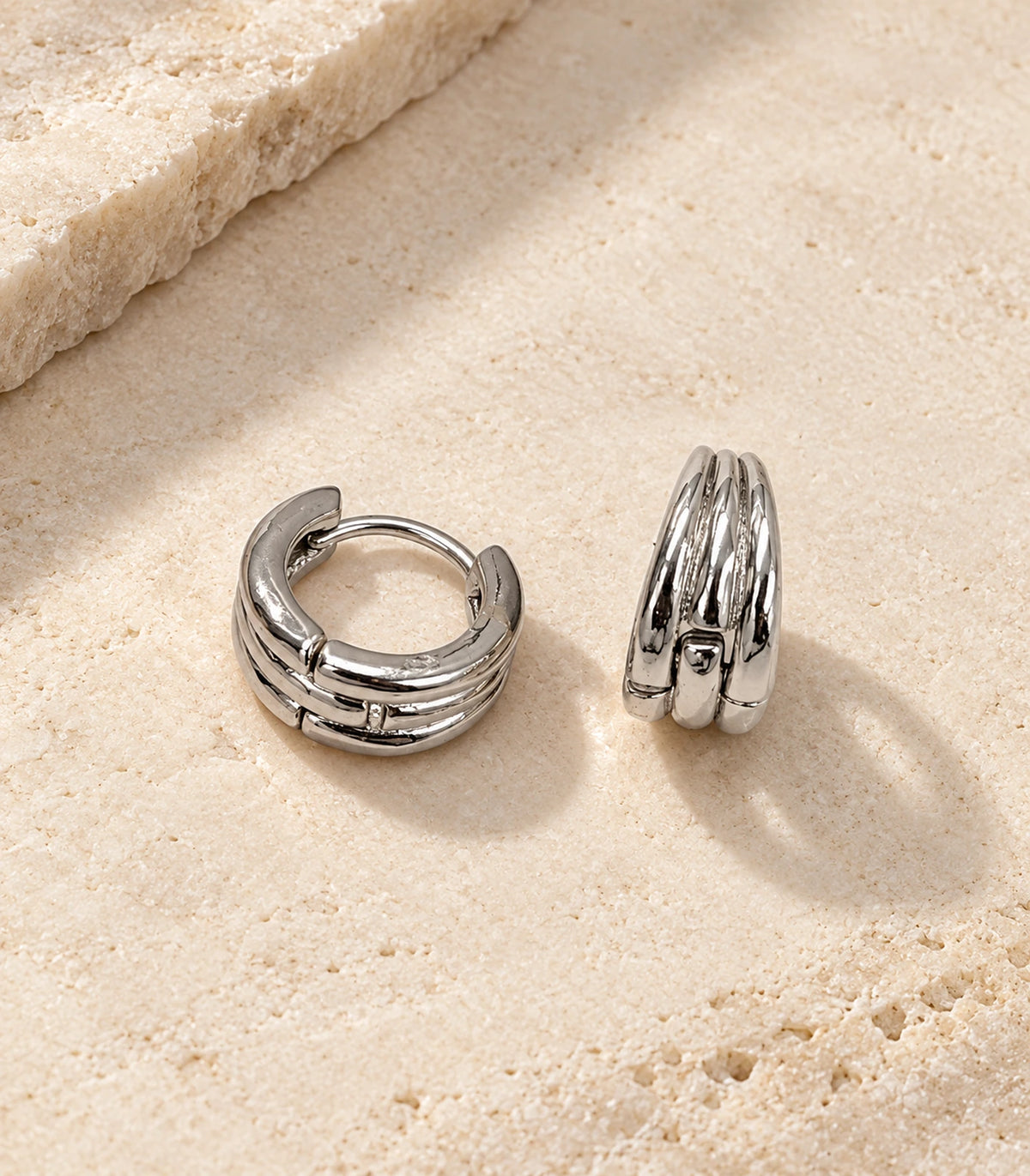 JIMIKI Triple-Ridge Huggie Hoop Earrings in Silver - editorial-flatlay #color_silver