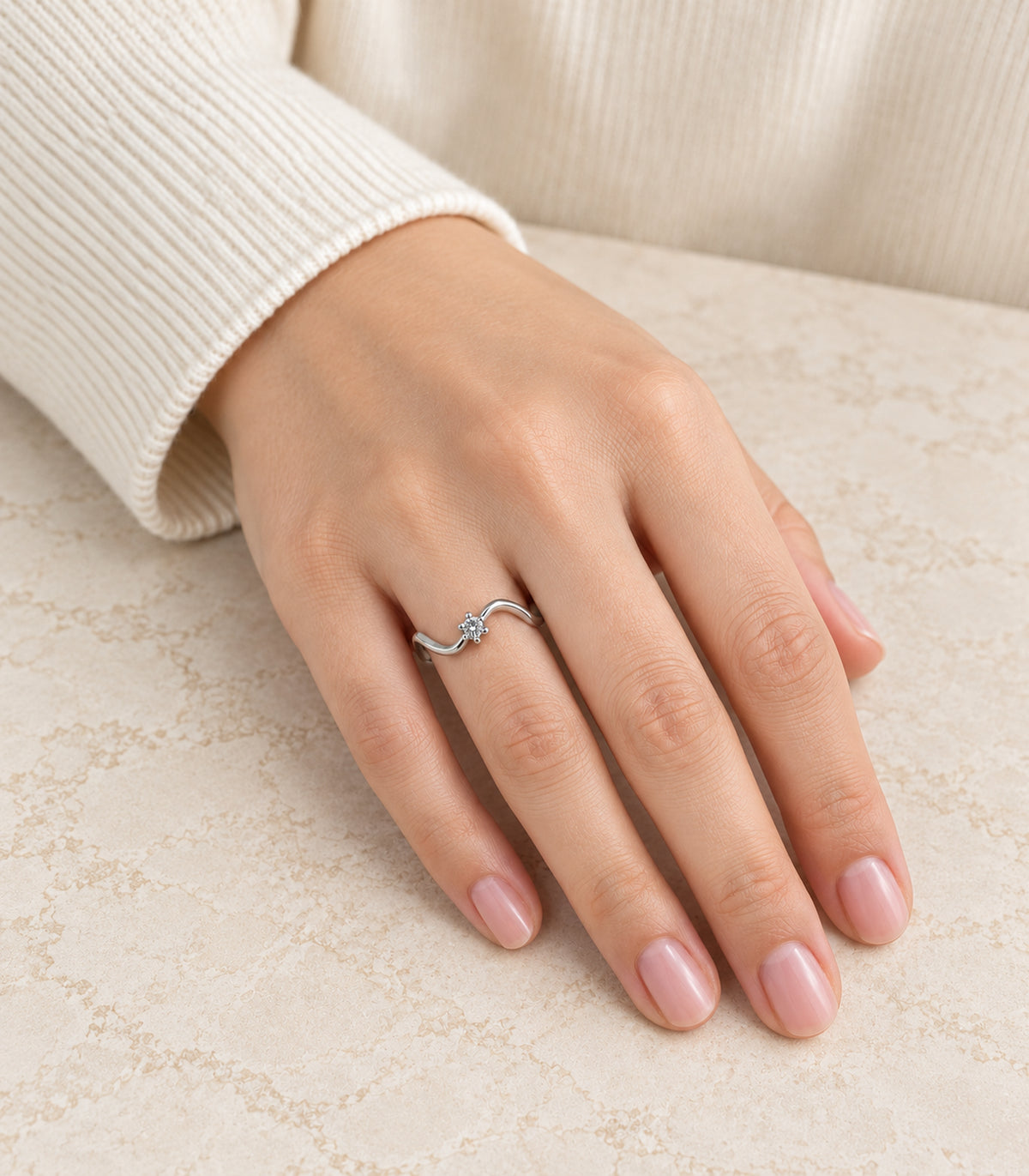 Silver-tone wave ring worn on a hand beside an ivory sleeve