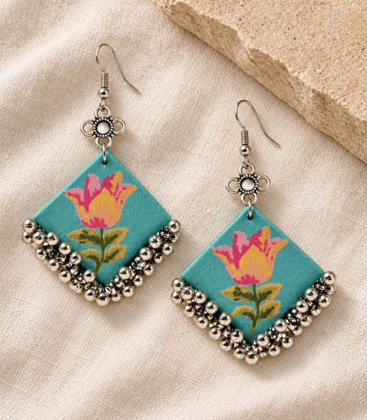 Matching pair of turquoise floral fabric ghungroo earrings on ivory linen