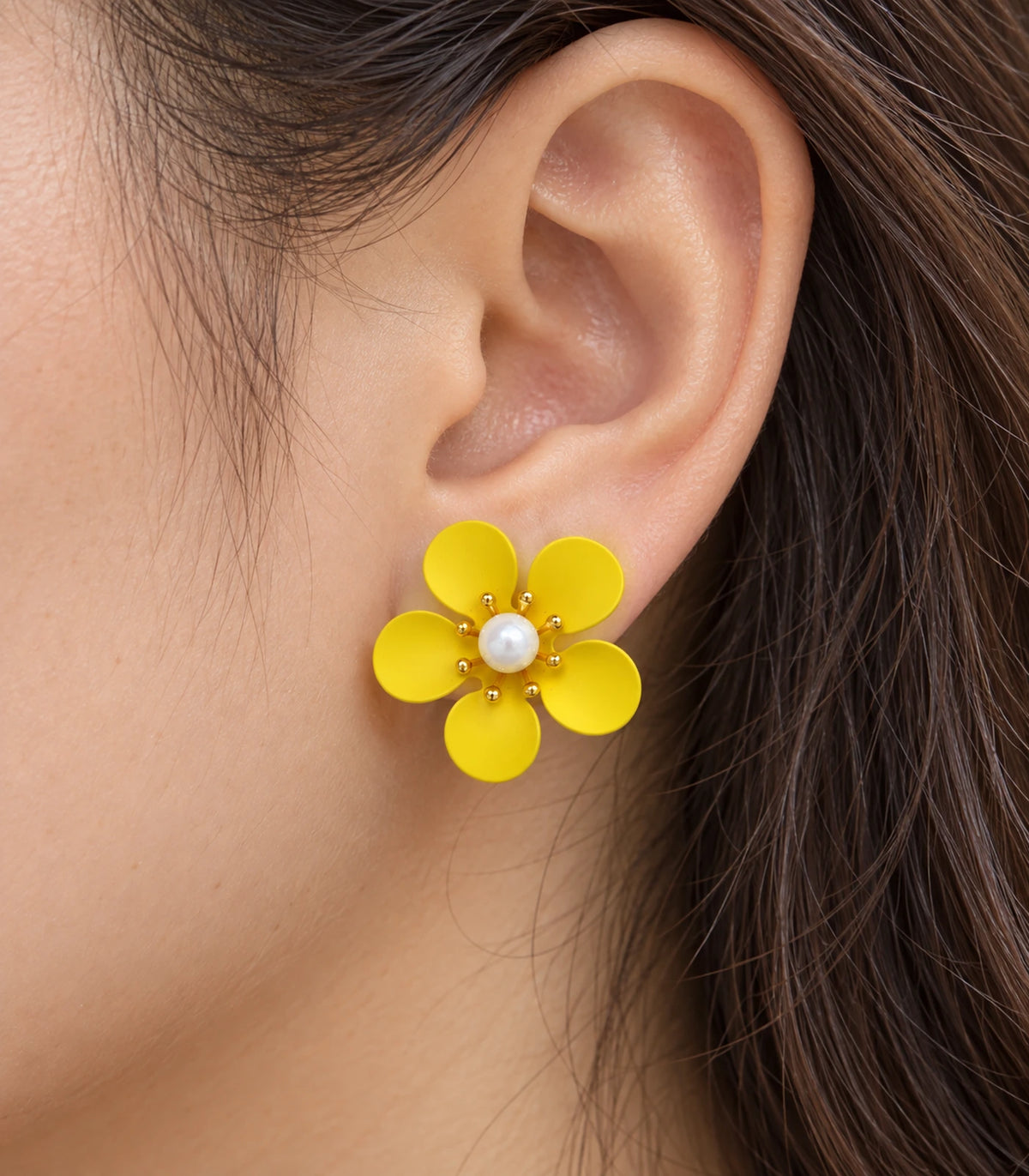 JIMIKI yellow five-petal flower stud earrings with pearl-effect centre, closeup of flower stud in a natural worn setting #color_yellow